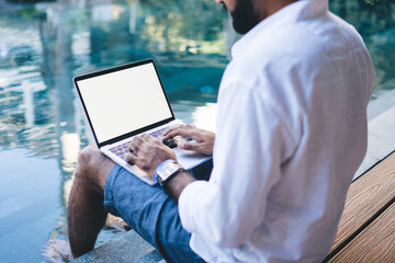Man working on laptop sitting near pool