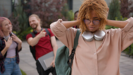 Group of angry students teenagers multiracial classmates mock humiliate bully mockery at college university outdoors discriminate thumbs down African American sad woman student stressed girl problem