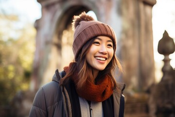 Fototapeta premium Portrait of a cheerful asian woman in her 30s sporting a trendy beanie on backdrop of ancient ruins