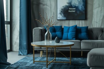 Modern and contemporary side tables with grey stone top on brass legs, near a gray sofa with blue pillows, in a minimalist living room.