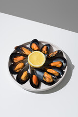 Plato de mejillones al vapor con limón sobre una mesa blanca y fondo gris