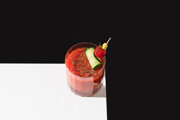 Cóctel Bloody Mary adornado con tomate cherry y pepino sobre una mesa blanca y fondo negro