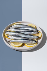 Anchoas frescas sobre rodajas de limón dentro de un plato sobre fondo blanco y azul