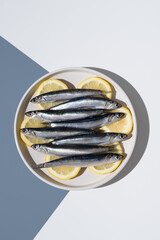 Anchoas frescas sobre rodajas de limón dentro de un plato sobre fondo blanco y azul. Vista superior