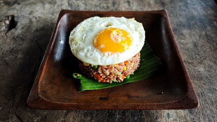 Delicious Indonesian fried rice topped with a sunny-side-up egg served on a rustic wooden plate with banana leaf garnish, perfect for traditional and natural-themed food presentations