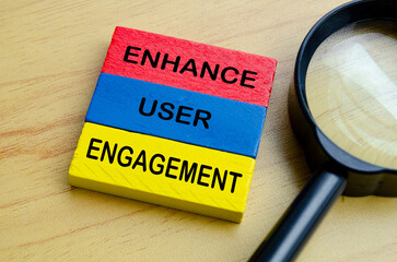 Top view of Enhance User Engagement text on multicolored wooden blocks with magnifying glass...