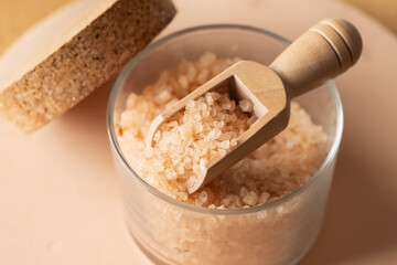 Close view of sea salt for relax bath in glass jare and wooden spoon on beige background.