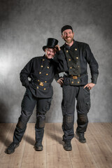 Schornsteinfegerin und Schornsteinfeger in Arbeitskleidung, gut gelaunt im Studio.