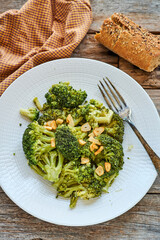 Sautéed broccoli with garlic on a white plate next to a checkered tablecloth on a rustic wooden table