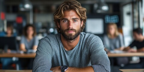 Obraz premium A contemplative bearded man with wavy hair sits confidently at a modern office workspace with blurred colleagues in the background, representing a professional work environment
