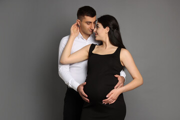 Beautiful pregnant woman with her husband on grey background