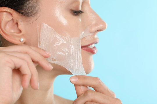 Beautiful woman peeling off face mask on light blue background, closeup - Powered by Adobe