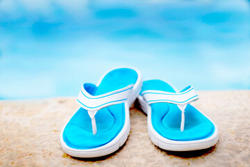 Obraz premium Blue Flip Flops Next to Swimming Pool Representing Summer Relaxation and Vacation