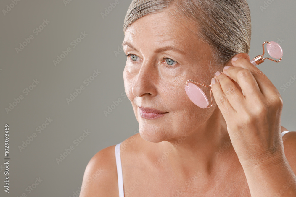 Poster Beautiful woman doing facial massage with roller on grey background