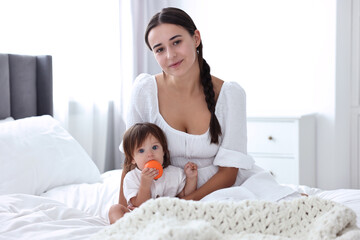 Beautiful young mother and her cute little baby with toy on bed at home