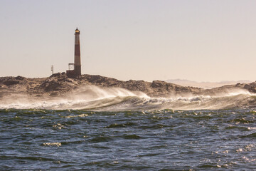 Silhouette of the lighthouse at Diaz point in Lüderitz, Namibia, at dawn, with wave breaking in...