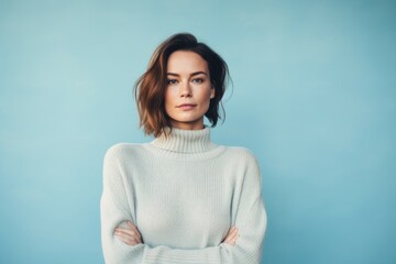 Obraz premium Portrait of a tender woman in her 30s dressed in a warm wool sweater while standing against pastel blue background
