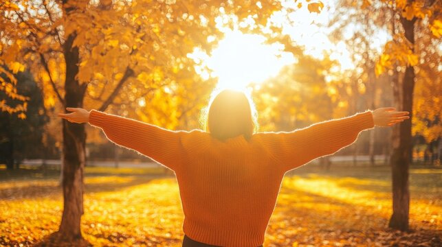 As the sun sets, a person stands in a park, arms outstretched, embracing the warmth of the golden autumn sunlight while surrounded by vibrant orange leaves.