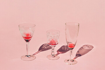 Glasses of wine and cocktails with red drinks and shadows on sunny day. Crystal glasses on pink background.