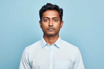 Fototapeta premium Portrait of a tender indian man in his 30s wearing a simple cotton shirt in front of pastel blue background