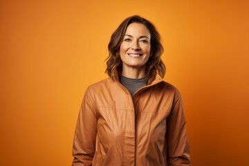 Fototapeta premium Portrait of a smiling woman in her 40s dressed in a water-resistant gilet in pastel orange background
