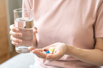 Sick, asian young woman, girl hand holding pill capsule, painkiller medicine from stomach pain, head ache, pain for treatment, take drug or vitamin and glass of water at home, pharmacy and health care