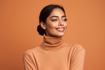 Portrait of a glad indian woman in her 20s wearing a classic turtleneck sweater over pastel brown background