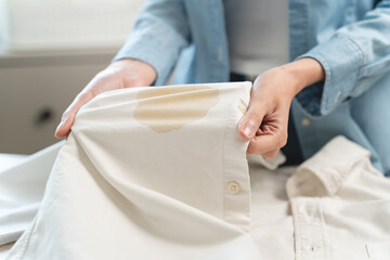 Housewife, asian young woman hand in holding shirt, showing making stain, spot dirty or smudge on clothes, dirt stains for cleaning before washing, making household working at home. Laundry and maid.