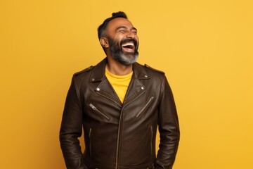 Obraz premium Portrait of a happy indian man in his 40s sporting a classic leather jacket isolated on soft yellow background