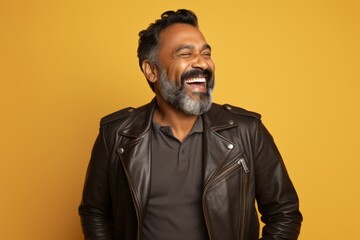 Obraz premium Portrait of a happy indian man in his 40s sporting a classic leather jacket in soft yellow background