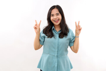 Positive successful Asian woman licks lips, makes victory gesture, shows two fingers, dressed in stylish shirt, poses indoor, rejoices success, isolated white background. Sign language