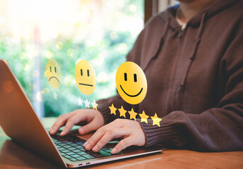Customer satisfaction rating and feedback concept. A person types on laptop, with smile face icons representing different satisfaction levels, customer reviews, feedback, and user experience rating.
