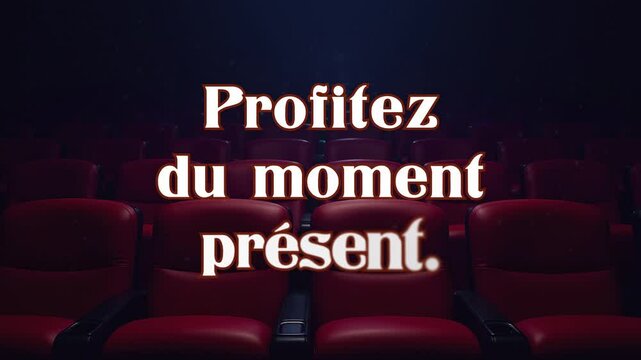 Text message appearing and dissolving on front shot of chairs in cinema: Profitez du moment pr&eacute;sent (French: enjoy the situation). Blue lighting above, floating dust particles.
