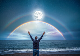 Full moon and double rainbow over ocean with man embracing nature