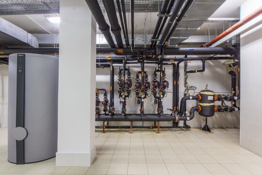 Industrial piping and control systems in a modern building utility room featuring valves and a cylindrical unit
