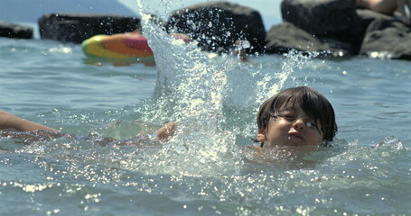 Child swimming in lake, water splashing in slow-motion at 800 fps, joyful summer day, rocks in...
