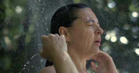 Close-up of woman under outdoor shower, water streaming down face in slow-motion at 800 fps, eyes...