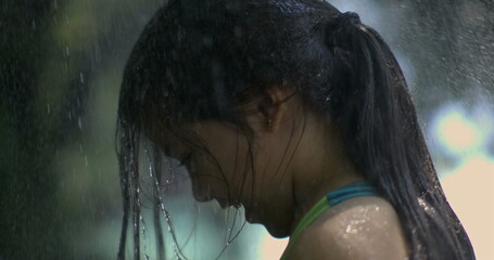 Slow-motion of a young girl with wet hair, head bowed, standing under pouring rain, evoking a mood...
