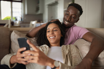 Young multiracial couple laughing at something on a phone at home