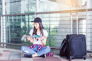 A young woman sitting on the floor of an airport terminal, reading a map beside her luggage. The image captures a moment of planning and exploration, ideal for travel and adventure themes.