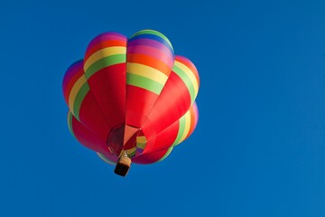 Naklejka premium A vibrant hot air balloon effortlessly soars against the backdrop of a clear blue sky in Oregon, USA. The striking colors of the balloon contrast beautifully with the serene, cloudless expanse, creati