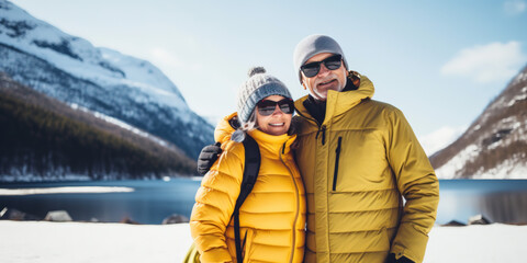 Senior couple 60 years old hiking among snowy mountains near a lake, Retiree travel and activities concept