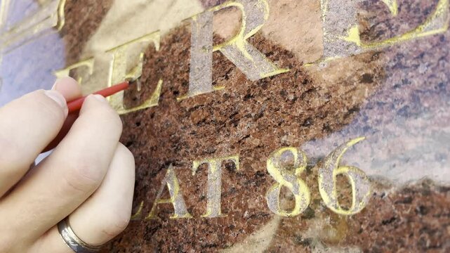 Renovation of golden letters text on a grave with some gold paint and brush