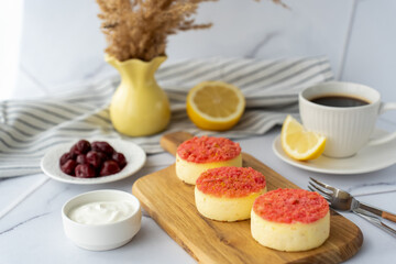 Delicious homemade cheesecakes with raspberry topping, served with sour cream, coffee, and cherries on wooden board for light breakfast in cozy kitchen. Homemade dessert and healthy breakfast options.