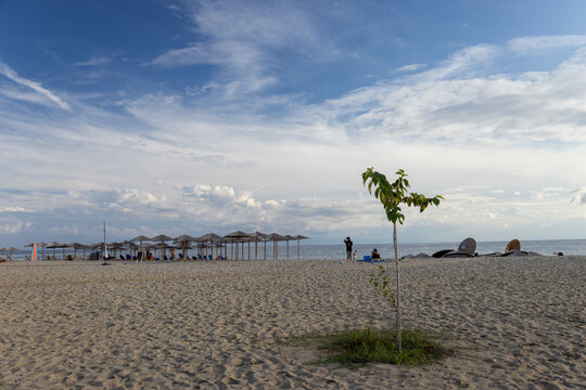 Nea Skioni, Greece, September 18, 2024--A serene beach with straw umbrellas, a calm sea, and people relaxing under a partly cloudy sky, capturing a peaceful and leisure-filled day at the coast.