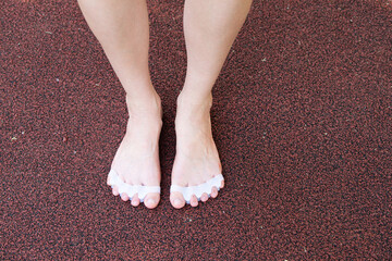 Close-up of female bare feet standing on a textured surface. The feet are wearing in silicone toe...