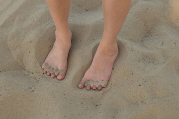 Female bare feet standing on sand, both feet wearing silicone toe separators to promote healthy toe...