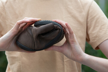 Women's hands hold twisted barefoot or anatomical brown shoes, demonstrating their flexibility and...