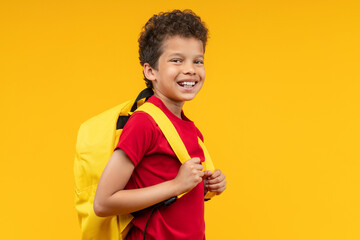 Studio portrait of happy smiling African American kid student posing over bright colored orange yellow background