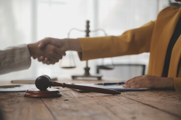 Lawyer shaking hands with a client making about documents, contracts, agreements, cooperation agreements with a female client at the lawyer's desk and a hammer at the table.